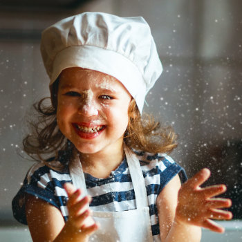a laughing child in a cooks costume spills flour