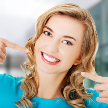 blonde girl with a beautiful smile points to her perfect teeth