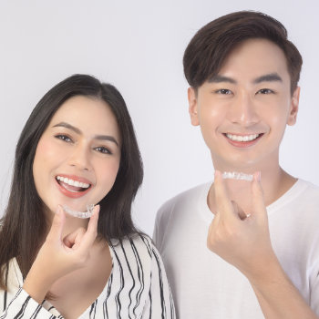 young smiling man and woman holding invisalign braces over white background