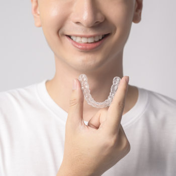 young smiling man holding invisalign braces over white background